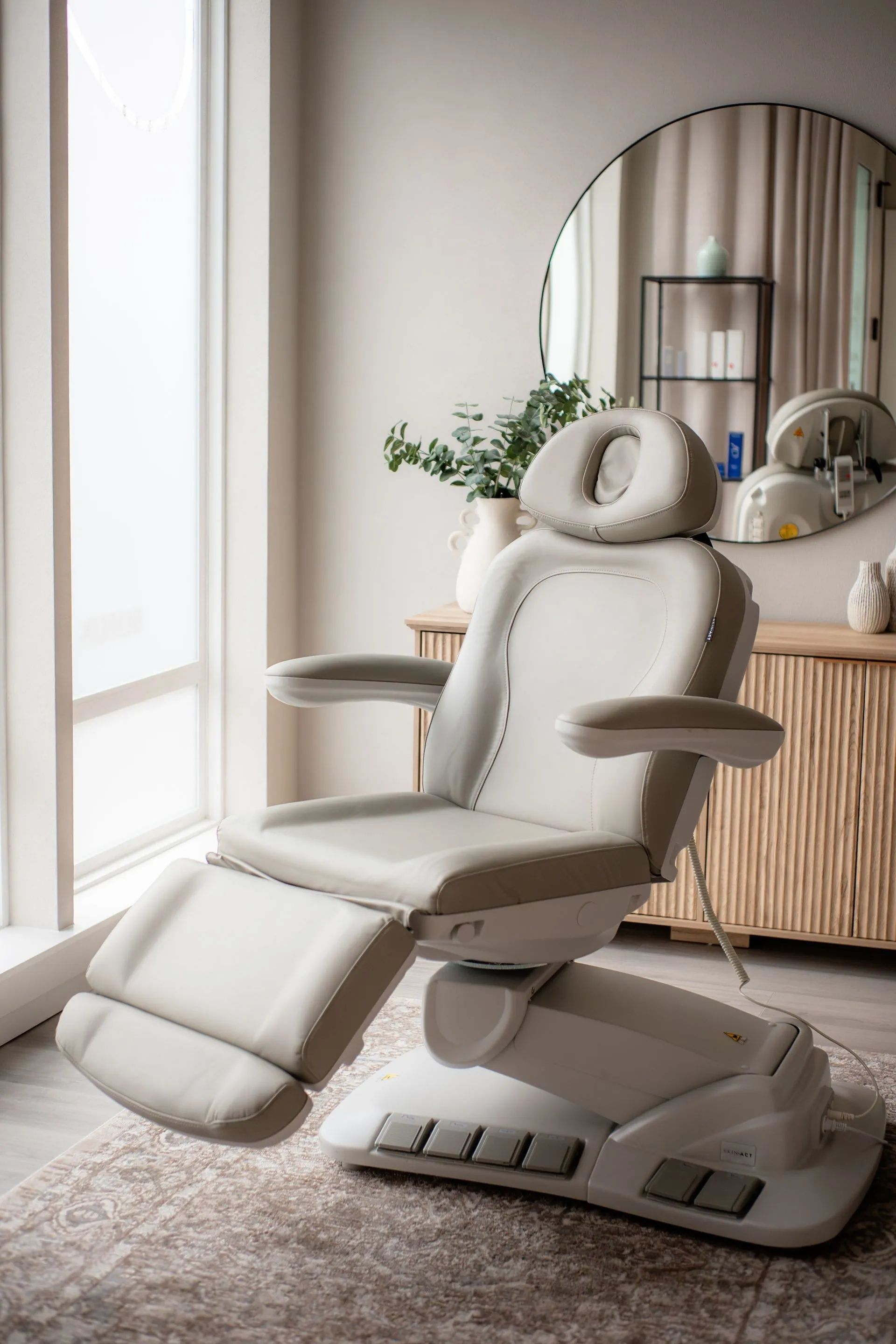 White reclining massage chair in a modern room beside a round mirror and wooden sideboard.