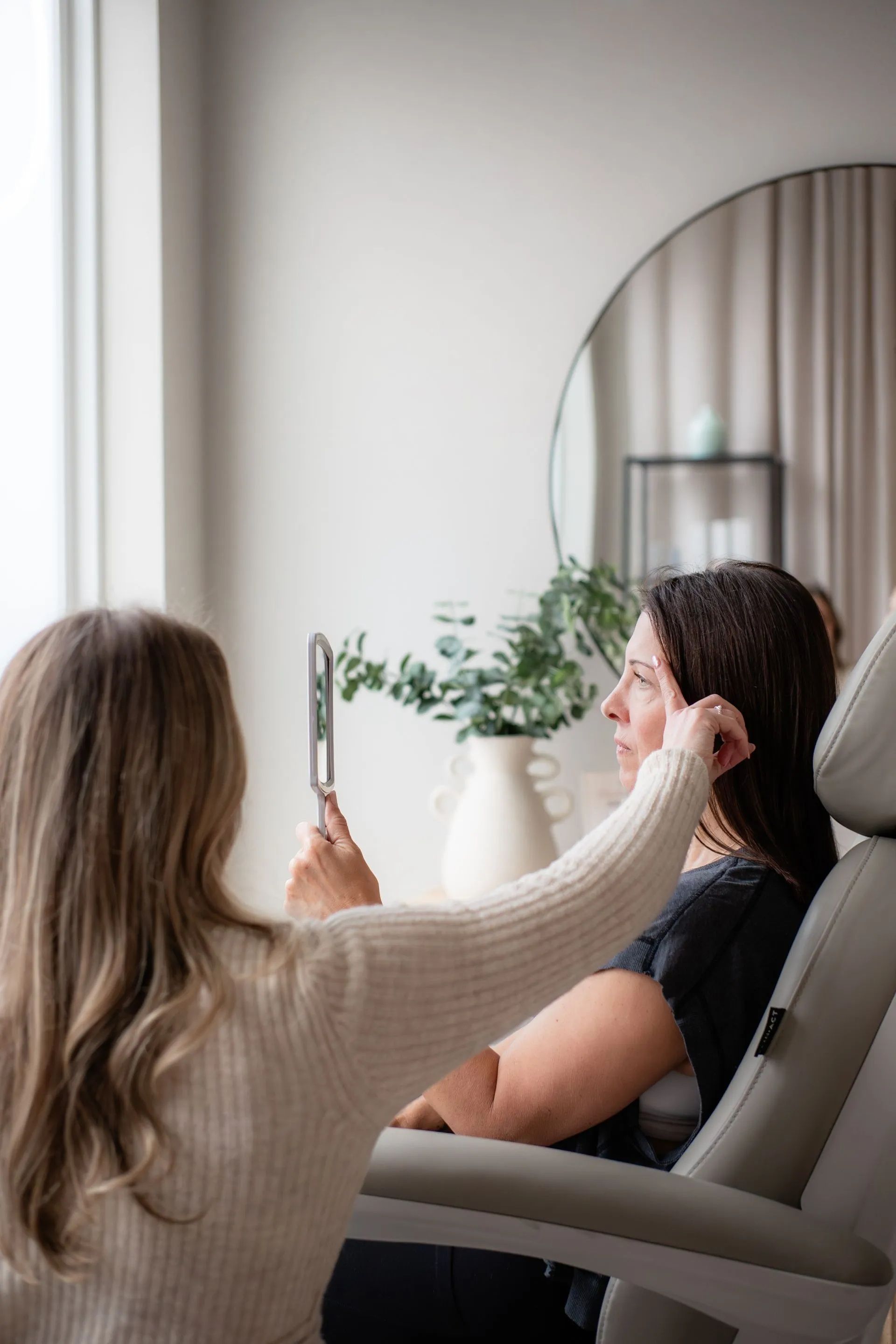 Person doing a video call on a smartphone in a bright living room, seated in a chair near a mirror.