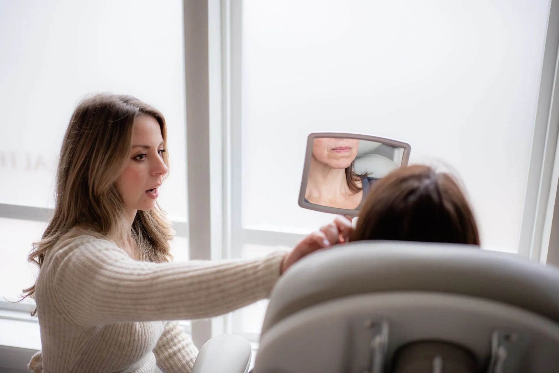 Woman showing a mirror to another person seated in a dental chair in a bright clinic