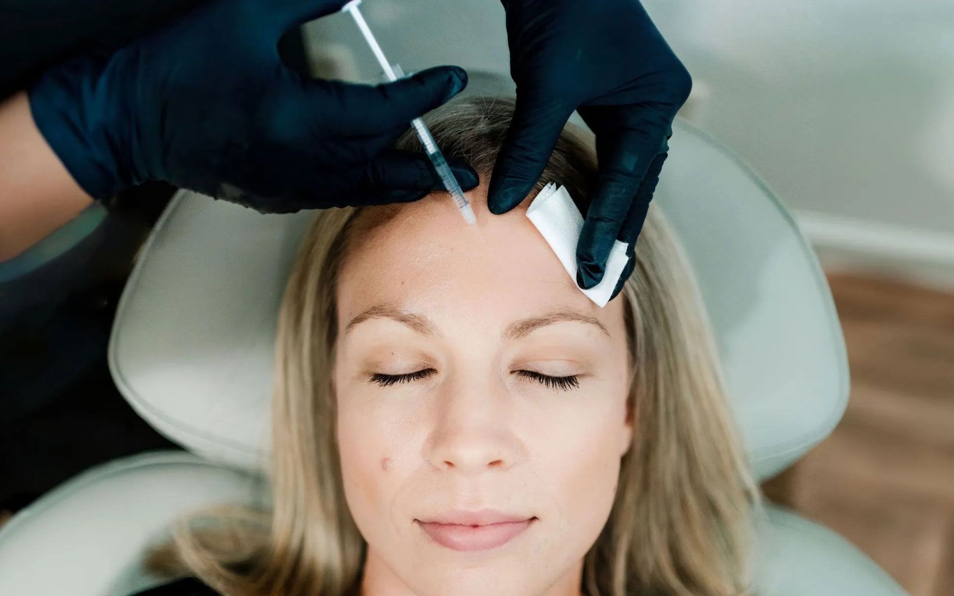 Gloved hands inject a woman’s forehead with a cosmetic syringe in a clinic