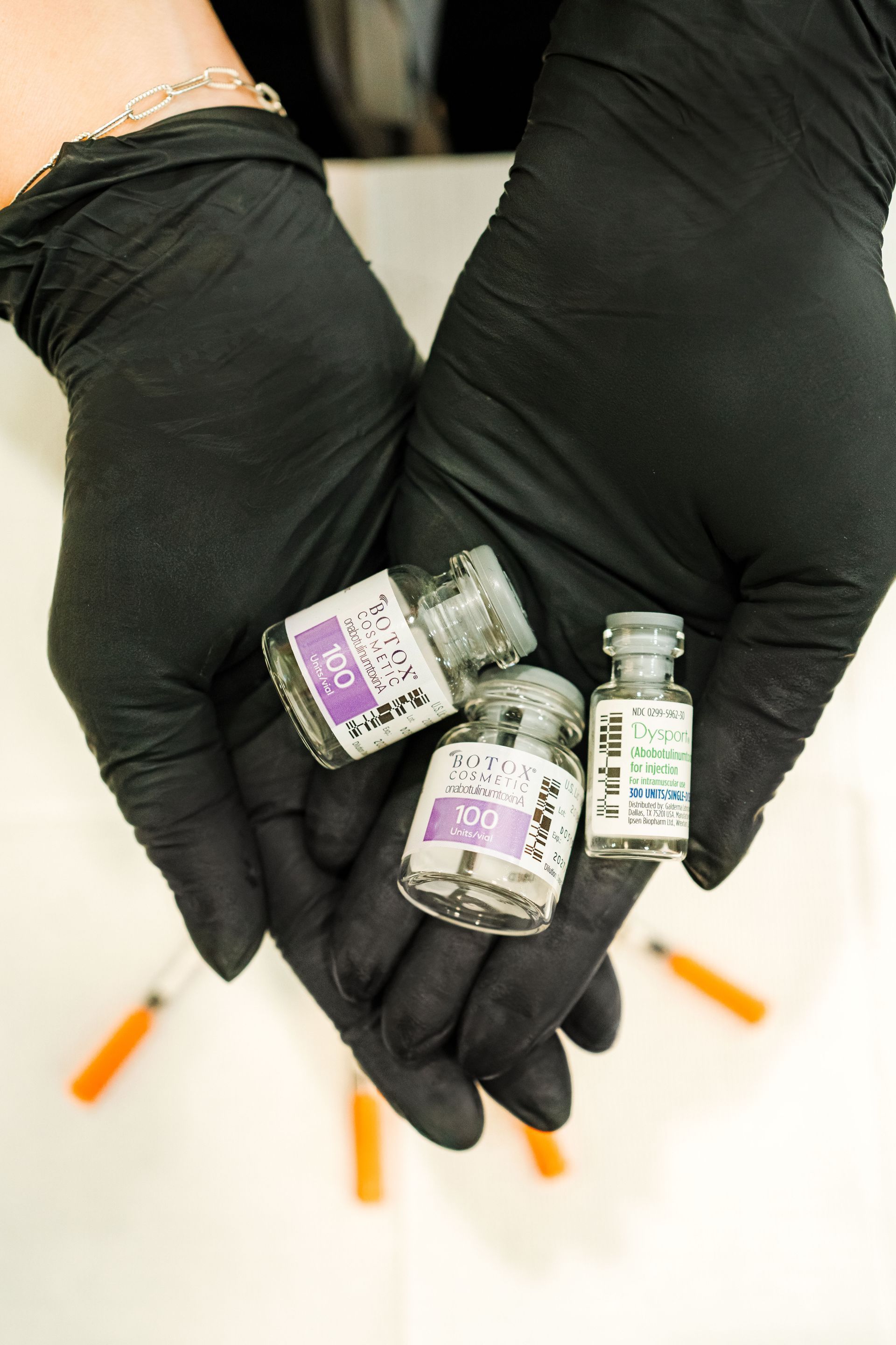 Gloved hands holding three small medicine vials on a white surface