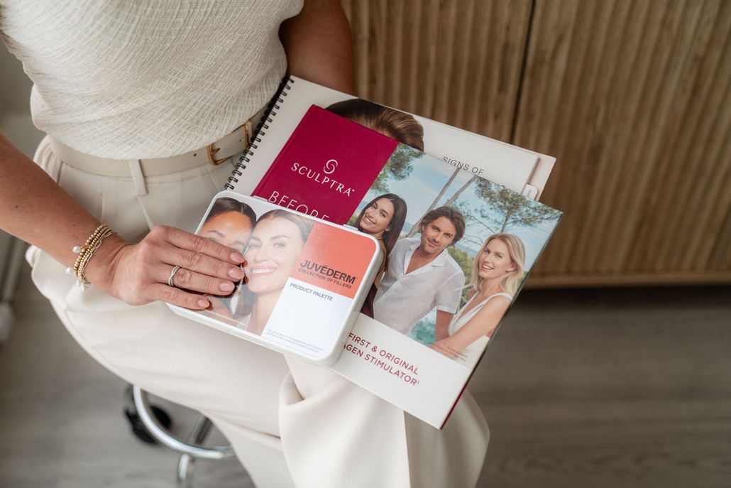 Person holding skincare brochures and product cards over white pants in a bright indoor setting