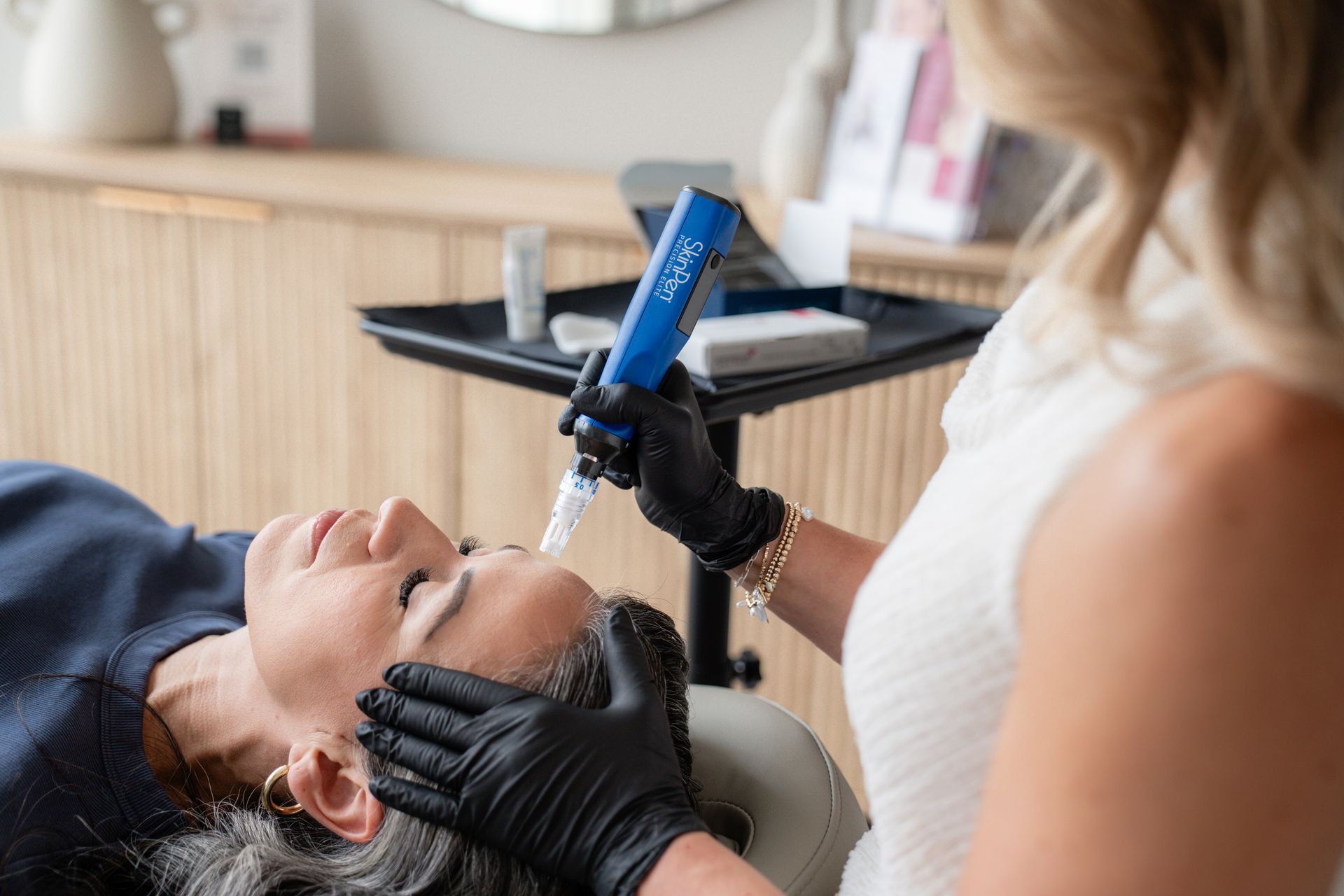 Cosmetologist using a blue handheld device on a client lying back in a spa treatment chair