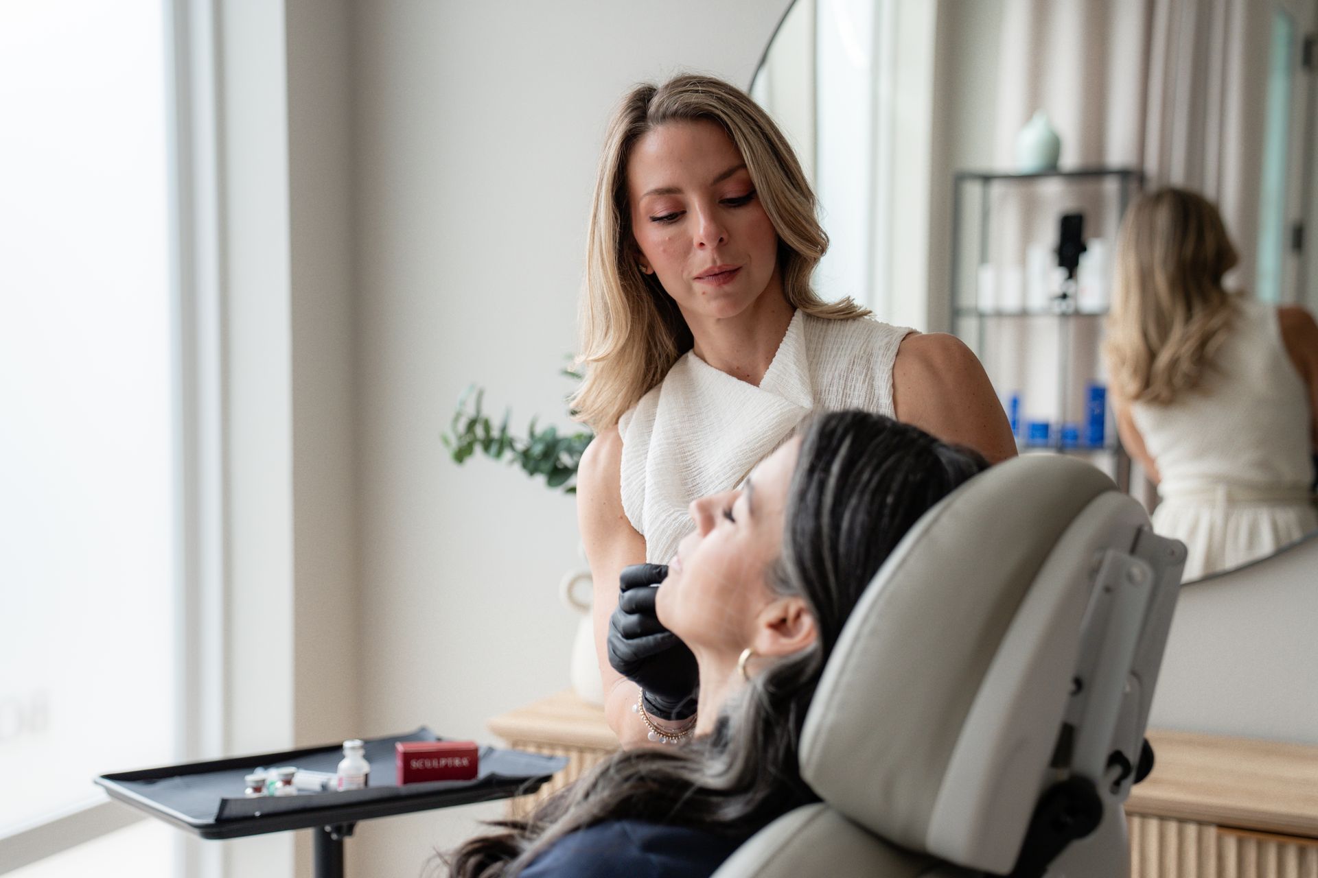 Woman giving a facial treatment to a reclining client in a bright spa room