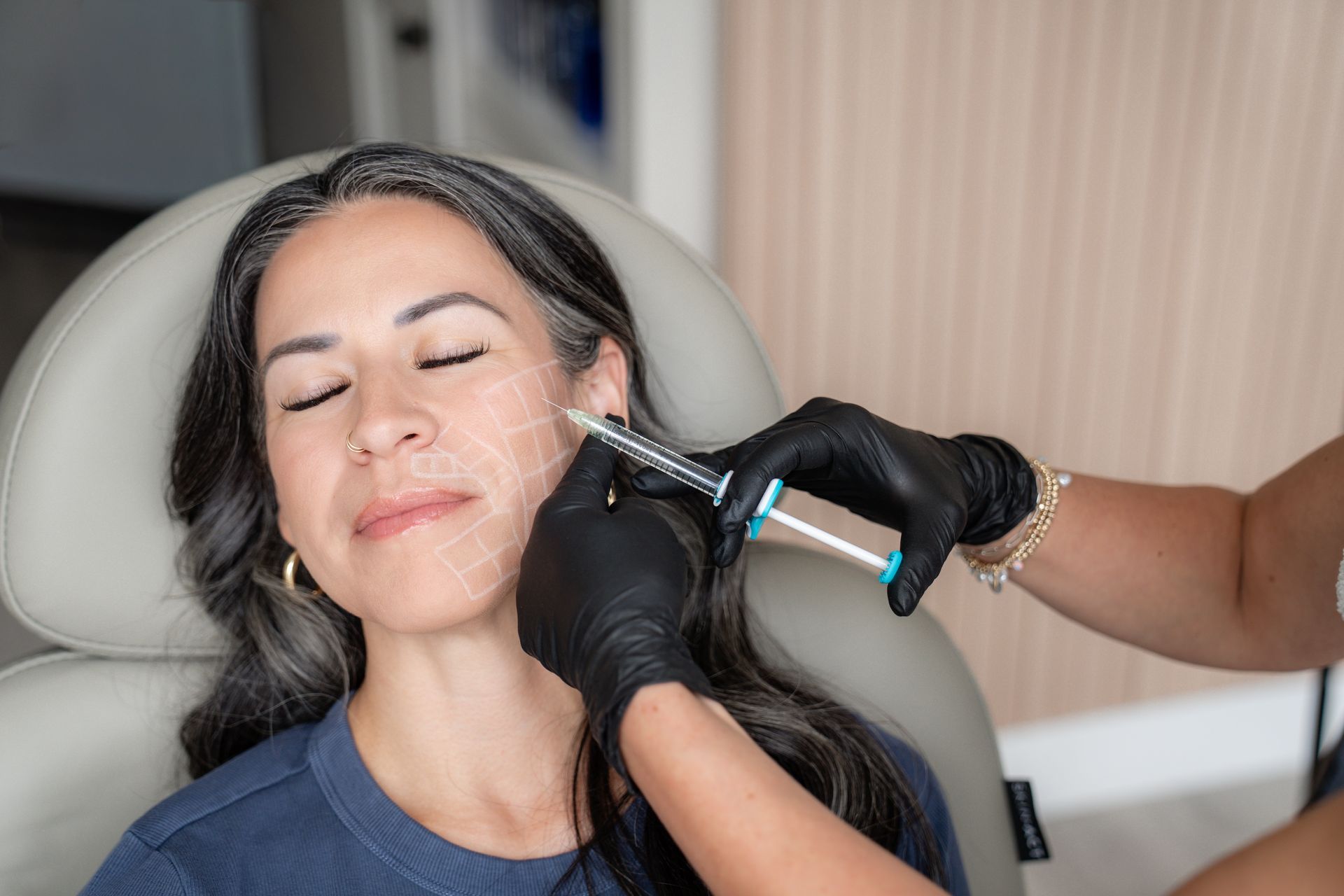 Woman receiving a facial treatment with a syringe-like device while reclining in a spa chair