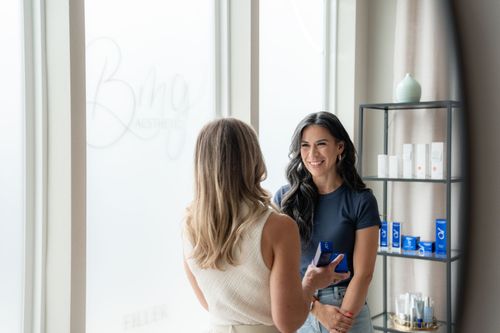 Two women talking in a bright spa, with product shelves in the background.