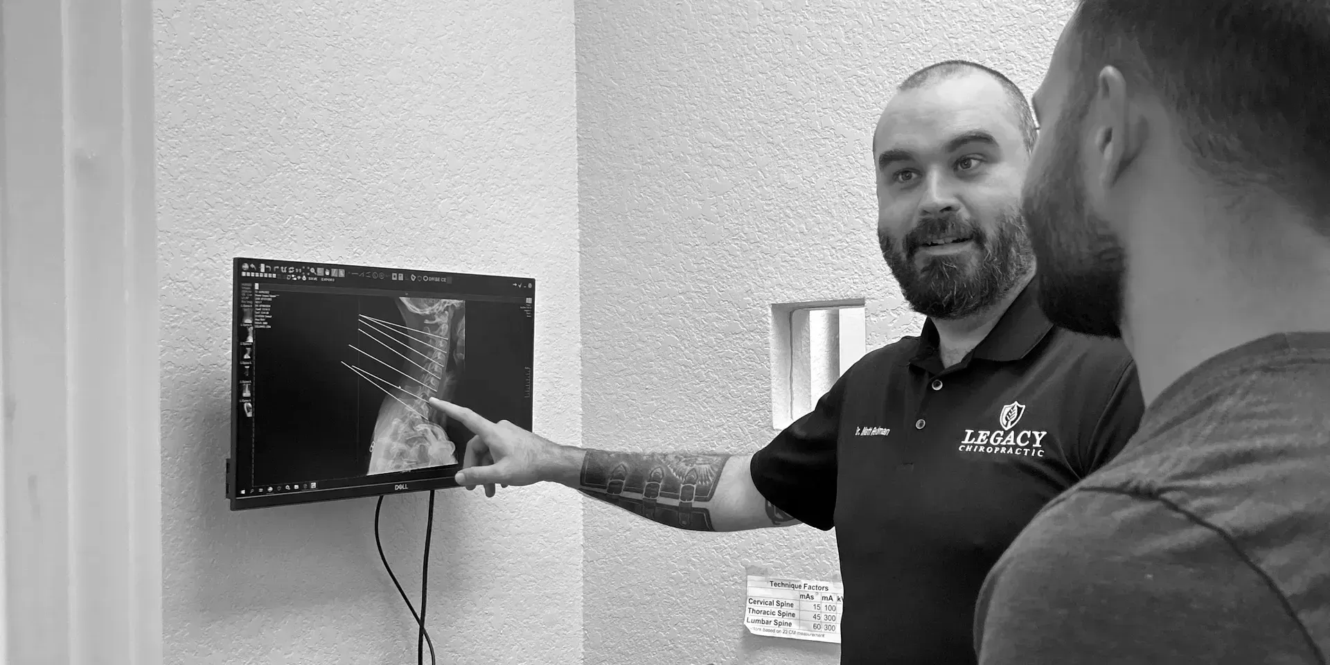 Man pointing at an x-ray on a monitor, explaining it to another person.