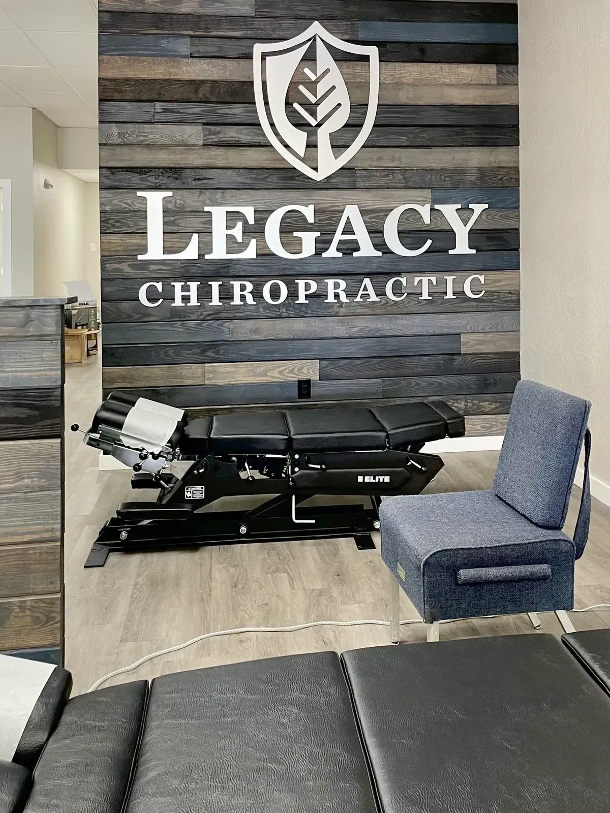 Chiropractic office interior with logo, adjustable treatment table, and blue upholstered chair.