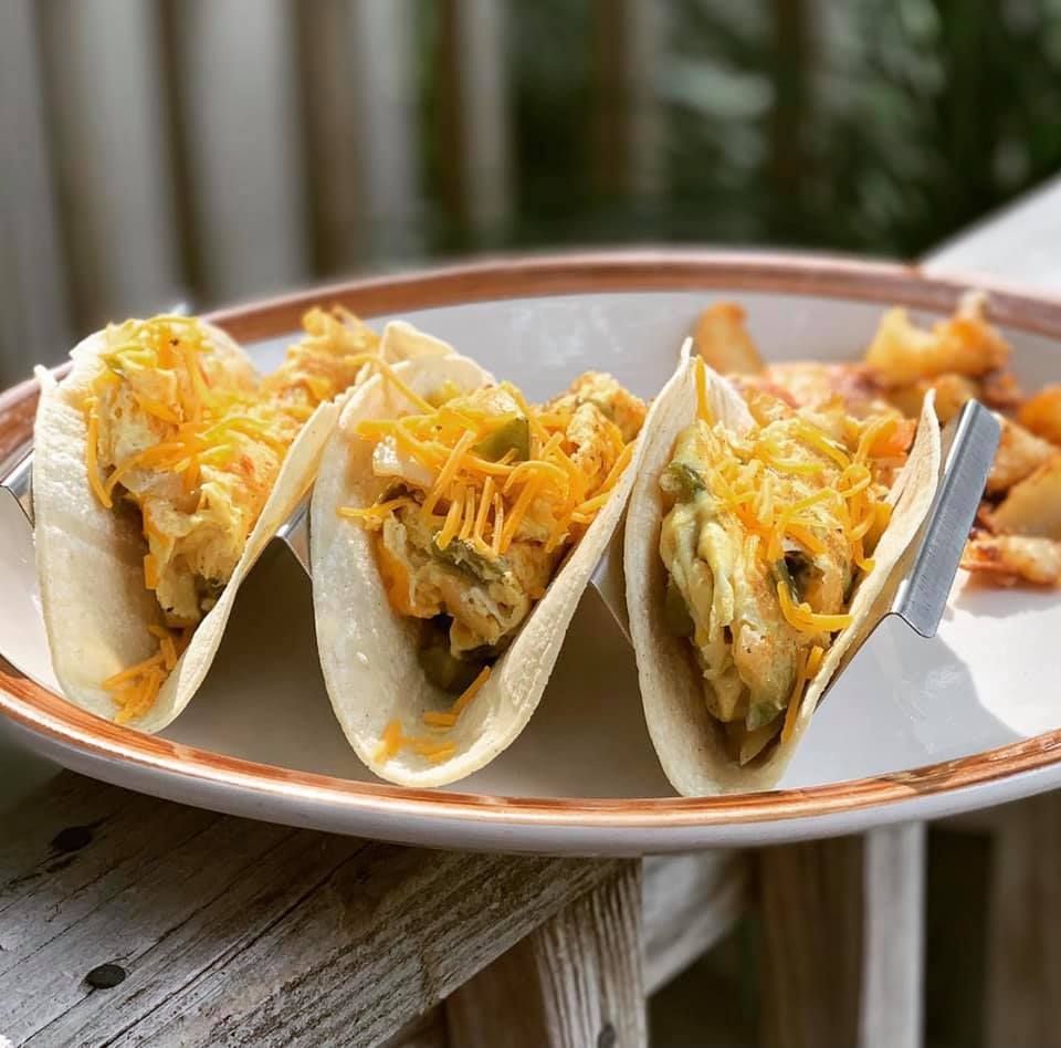 Three tacos with shredded cheese, with a side of fried potatoes.