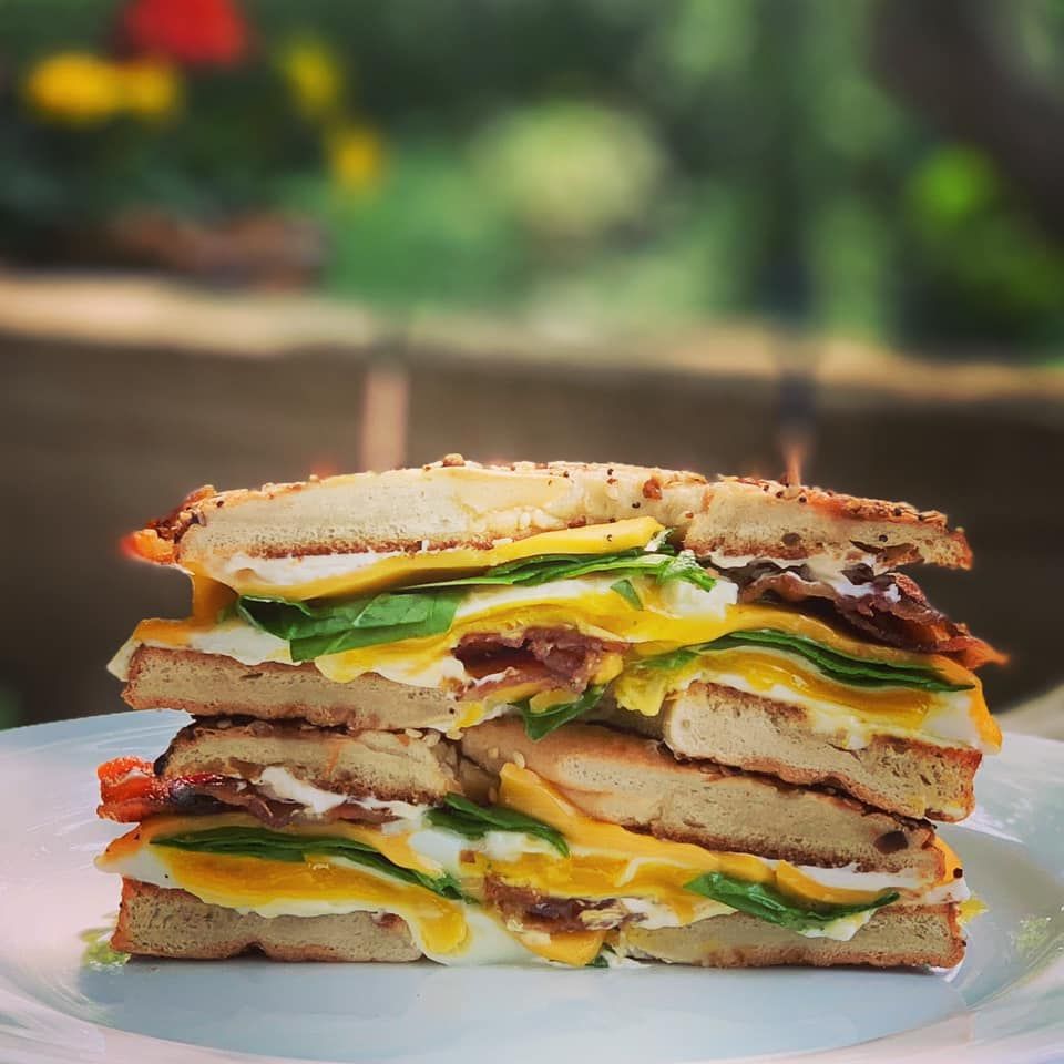 Stacked sandwich with eggs, bacon, cheese, and spinach on a white plate, outside.