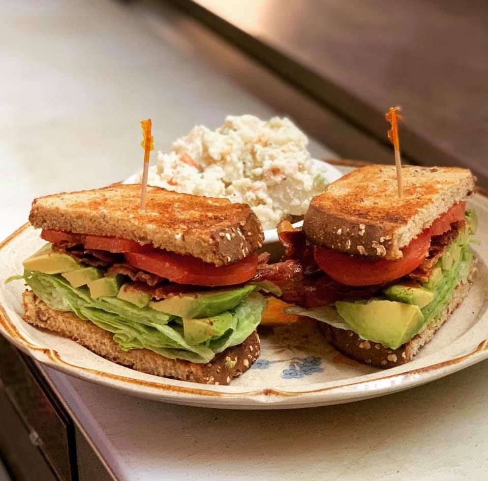 Club sandwich with bacon, avocado, tomato, and lettuce, served with coleslaw.