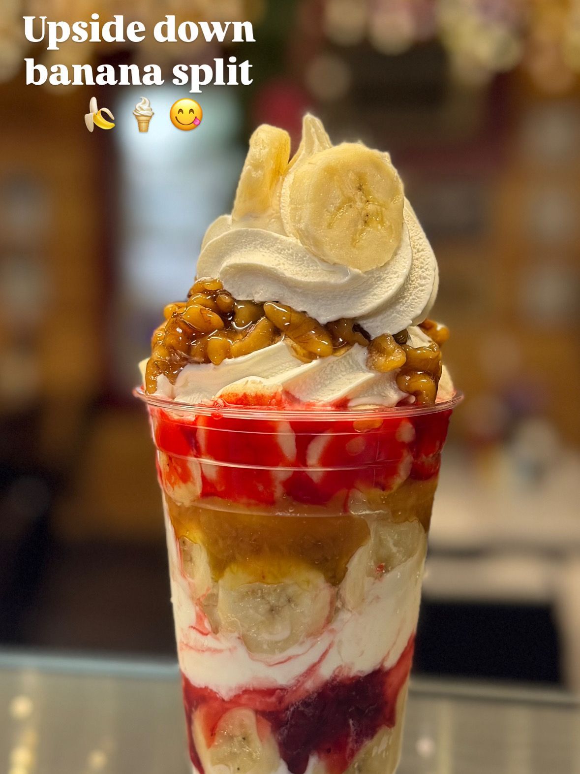Upside-down banana split dessert in a clear cup with whipped cream, bananas, and red syrup