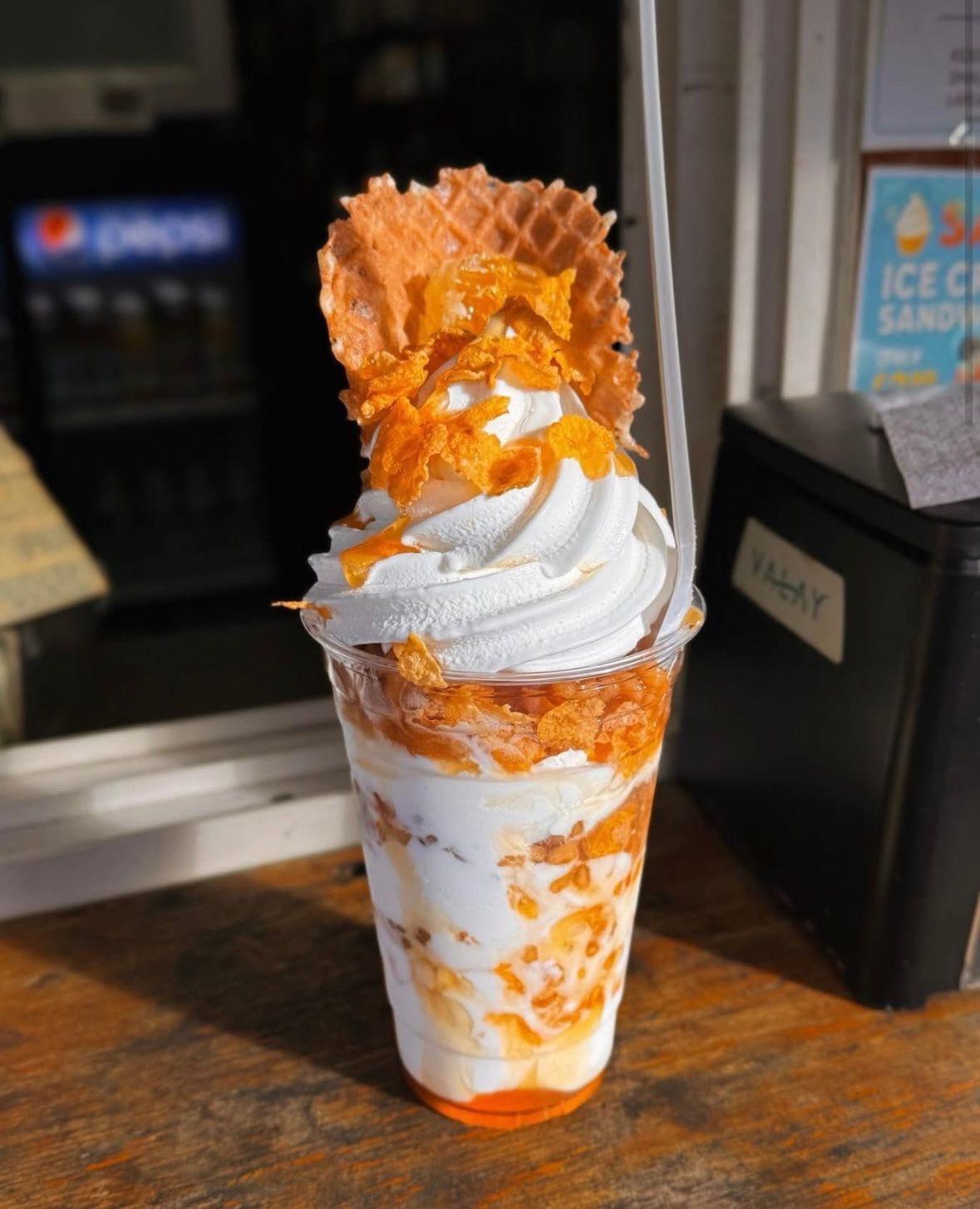 Tall dessert cup with vanilla soft serve, orange syrup, and waffle pieces on a counter
