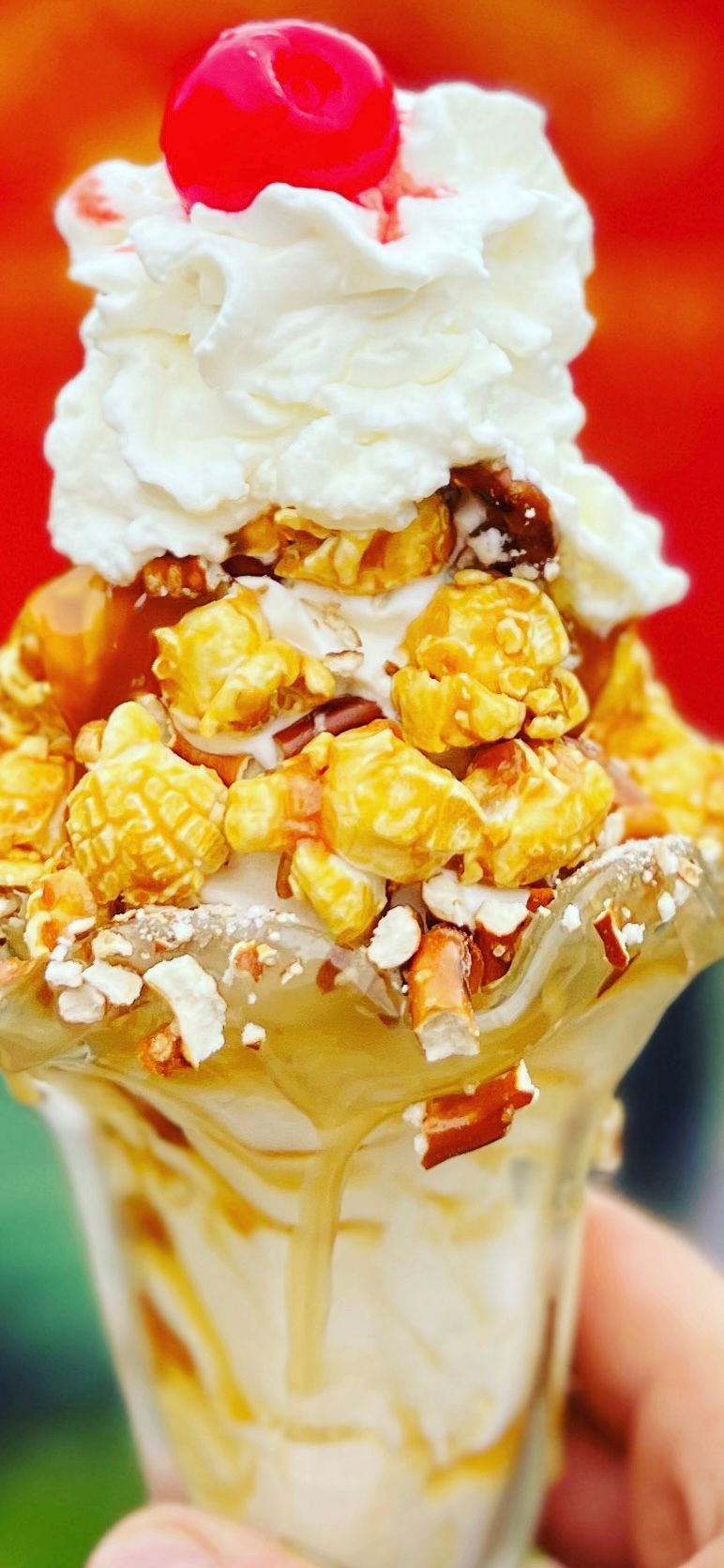 Tall ice cream sundae in a glass with whipped cream, caramel drizzle, and a red cherry on top