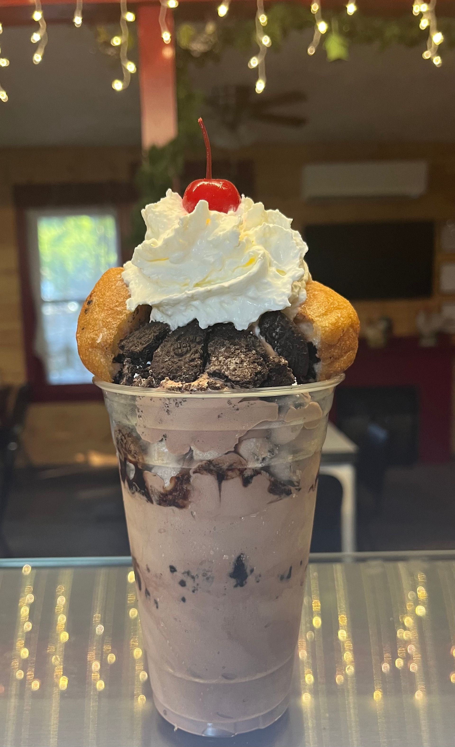 Tall milkshake topped with whipped cream, cherry, cookies, and a wafer in a dimly lit café
