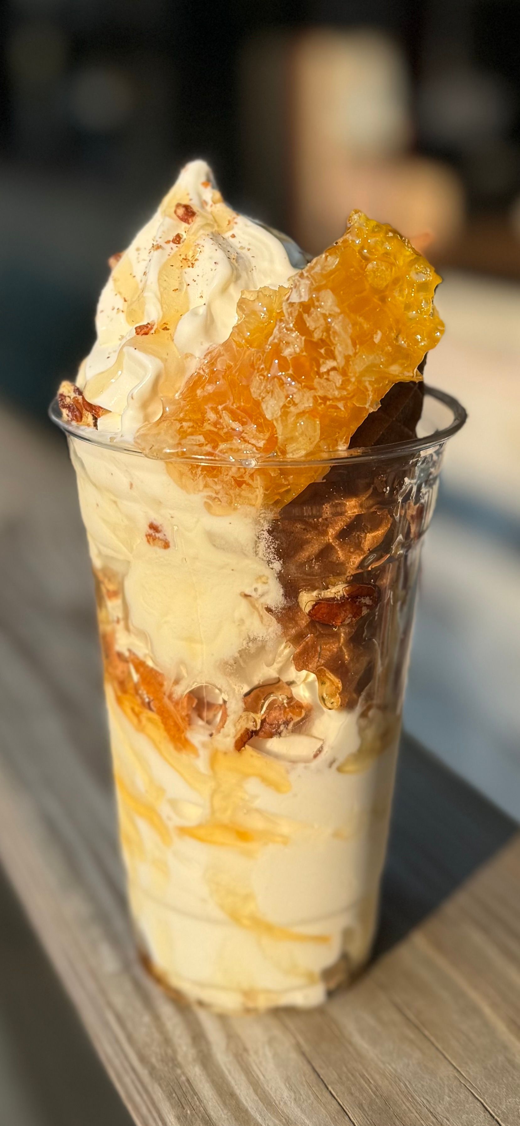 Tall iced dessert drink topped with whipped cream and amber syrup in a clear cup on a table