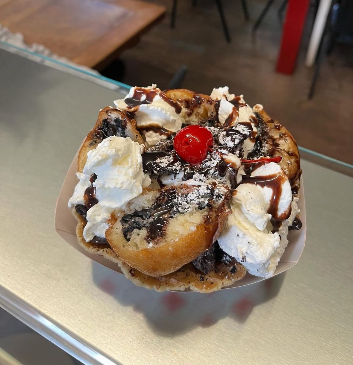 Dessert sundae with whipped cream, chocolate drizzle, and a cherry on top in a paper cup