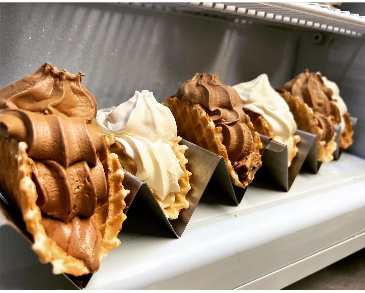 Row of chocolate and vanilla soft-serve cones in black paper holders on a display tray