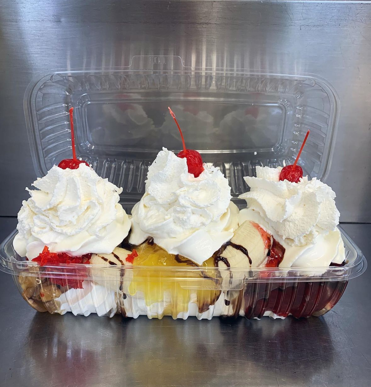 Three dessert cups topped with whipped cream and cherries in a clear plastic container
