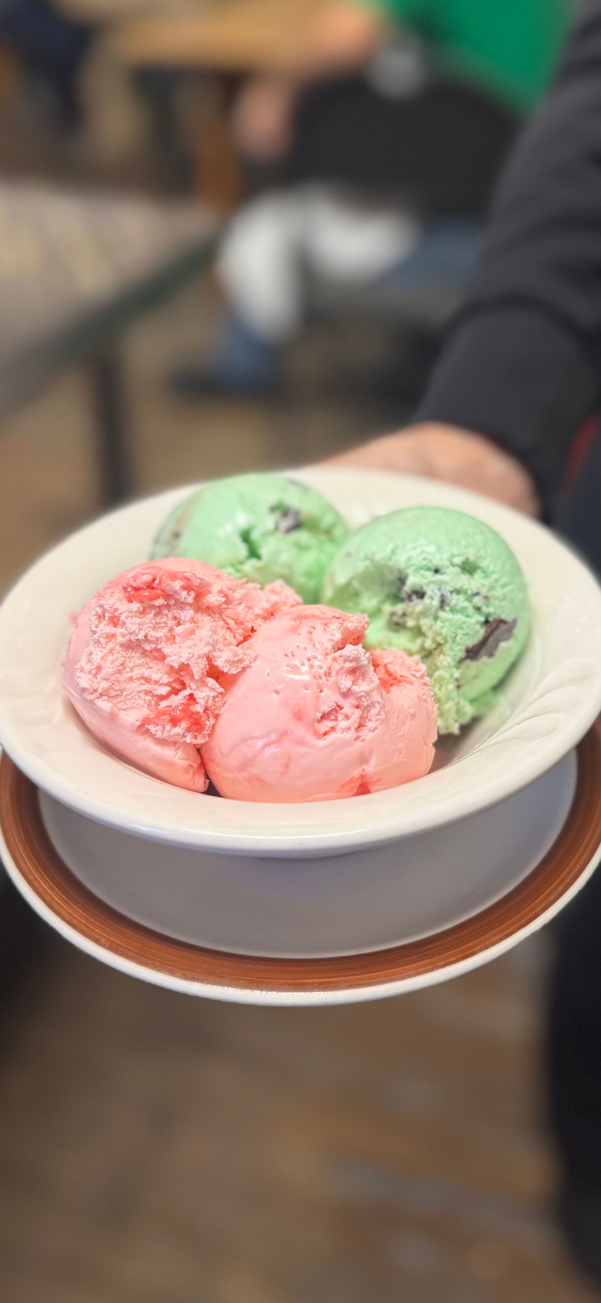 Three scoops of pink and green ice cream in a white bowl on a table