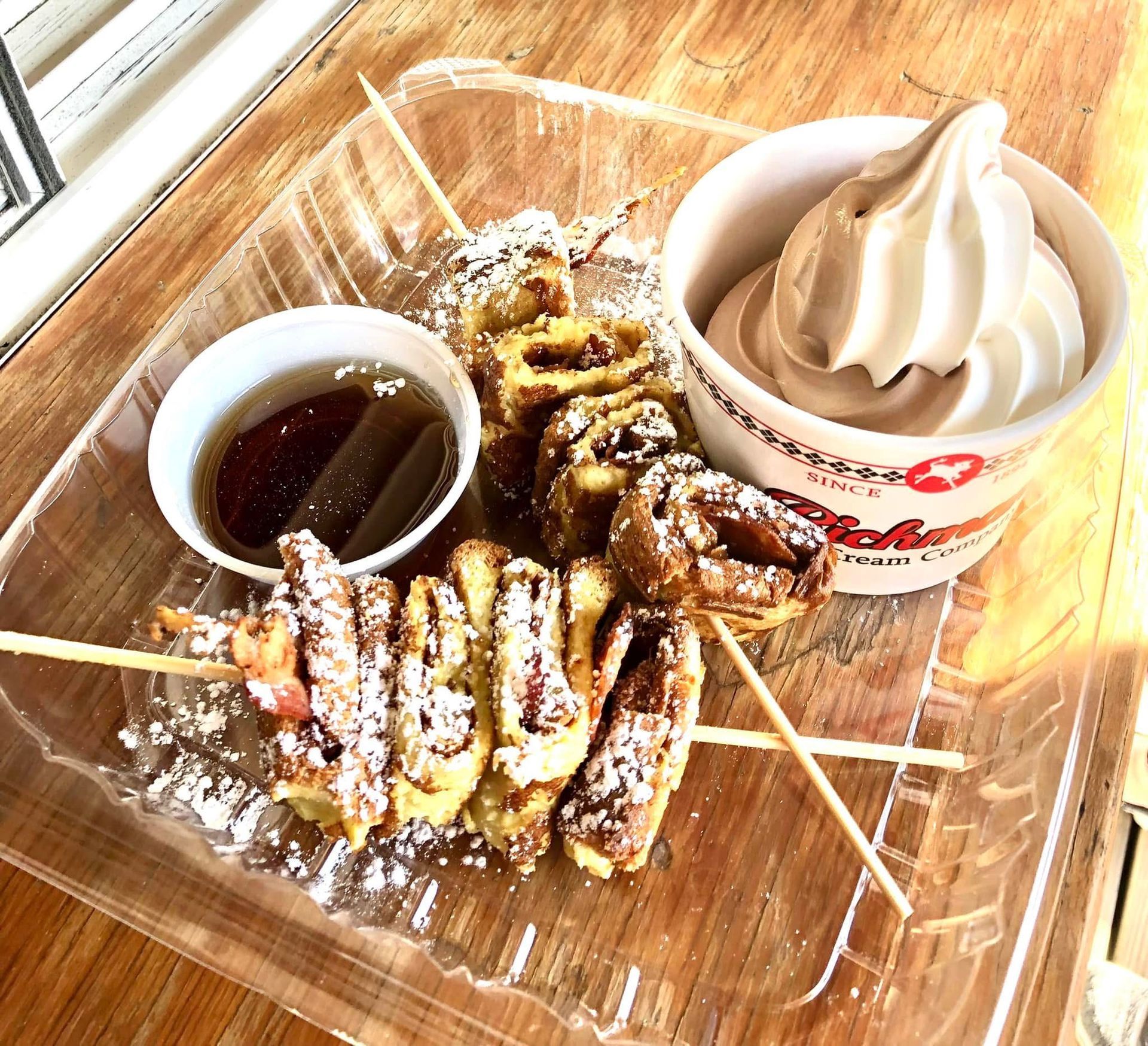 Dessert platter with skewered pastries, chocolate sauce, and soft-serve ice cream on a wooden tray