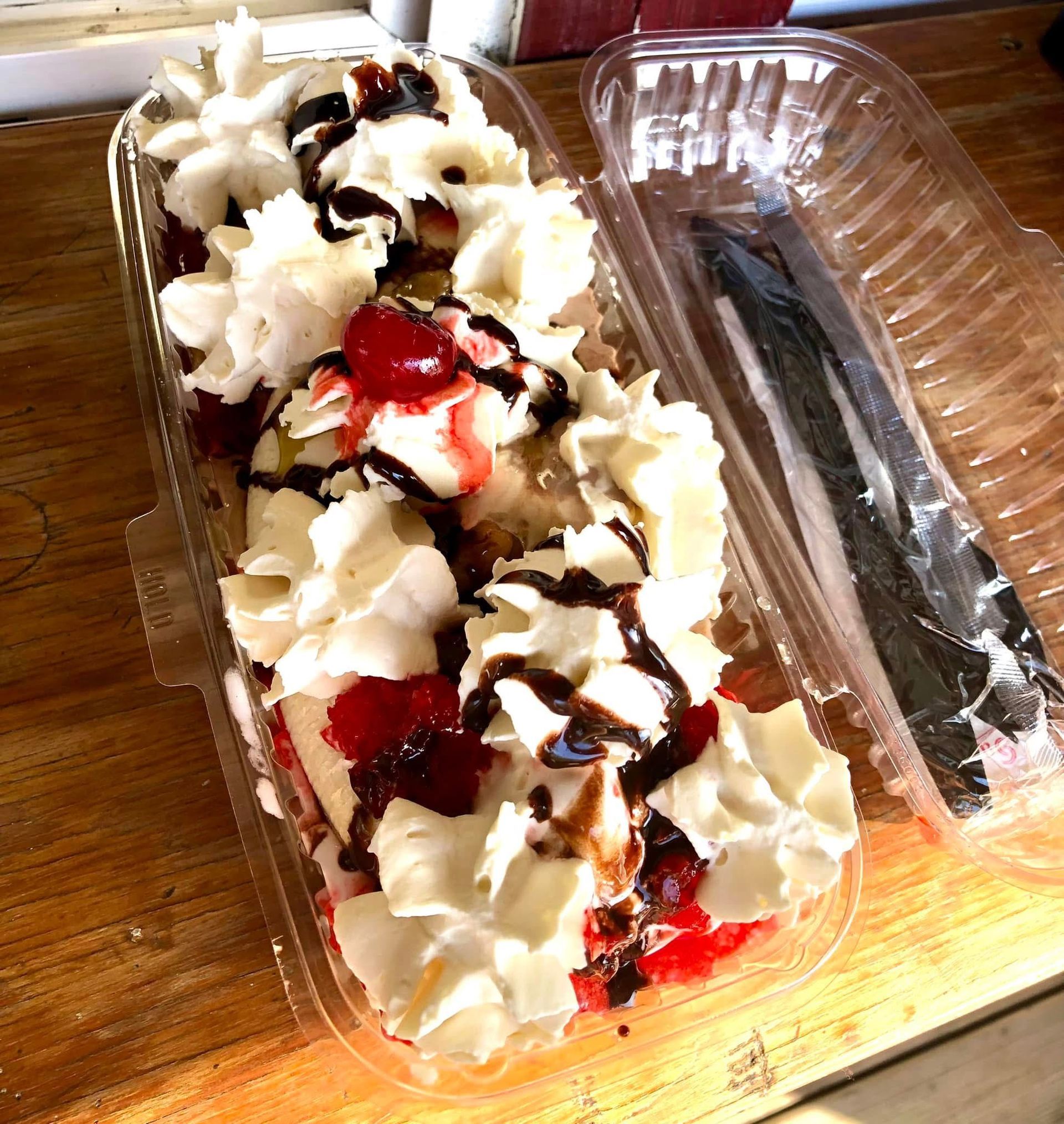 Dessert in a clear clamshell container, topped with whipped cream, strawberry sauce, and chocolate drizzle.