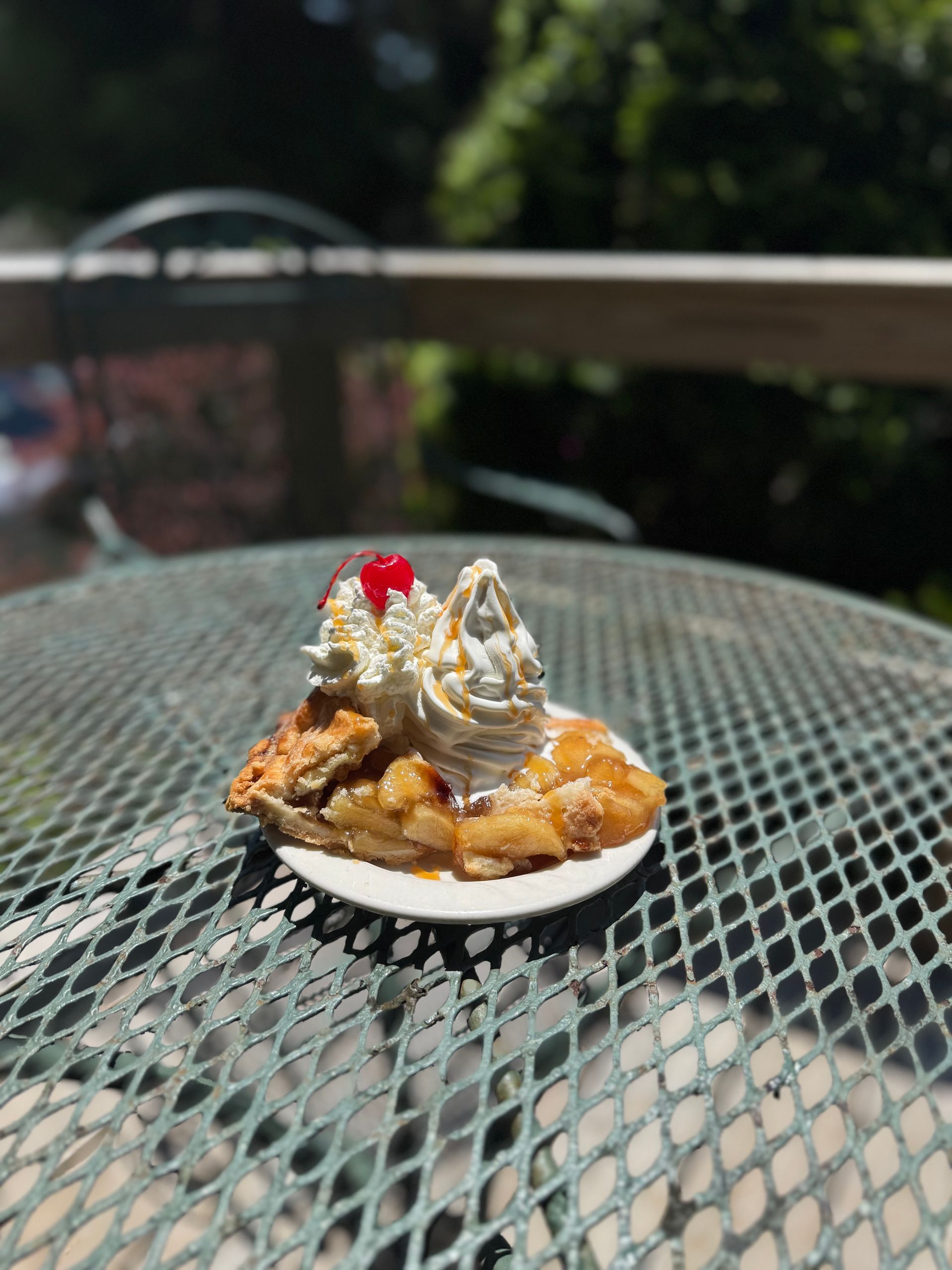 Dessert topped with whipped cream and a cherry on a white plate on a metal patio table