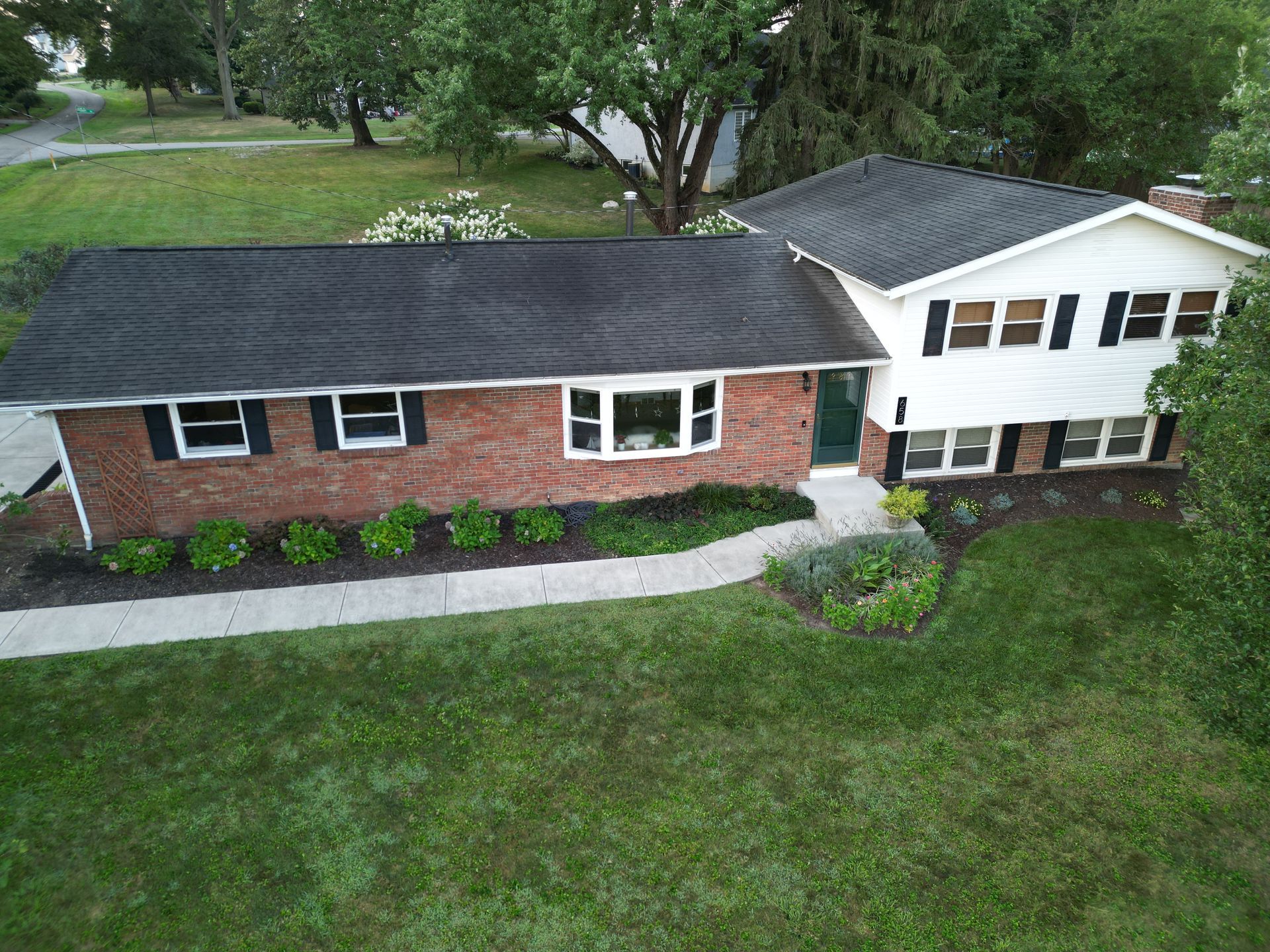An aerial view of a brick house with a black roof and white trim.