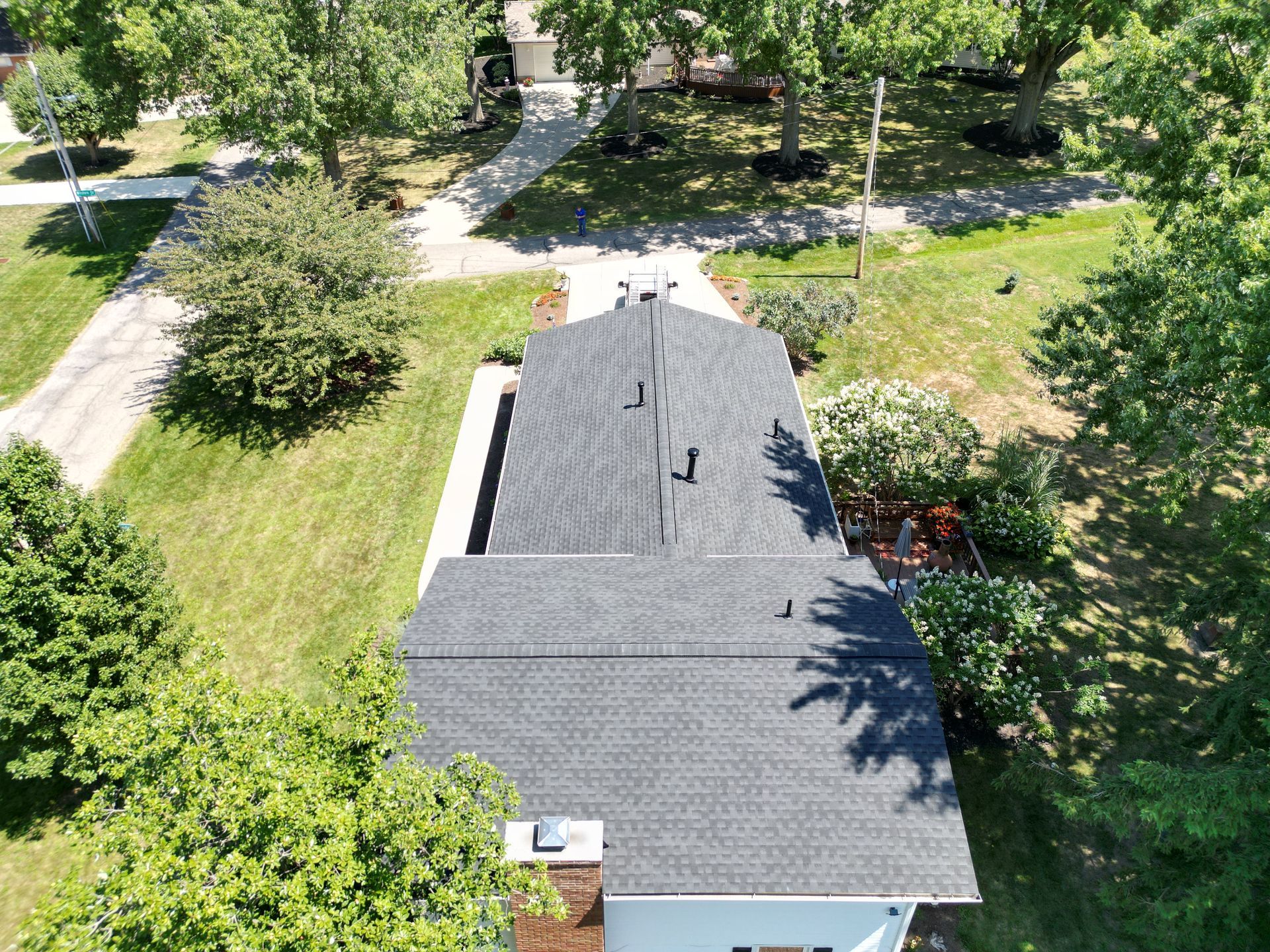 An aerial view of a house with a black roof surrounded by trees and grass.