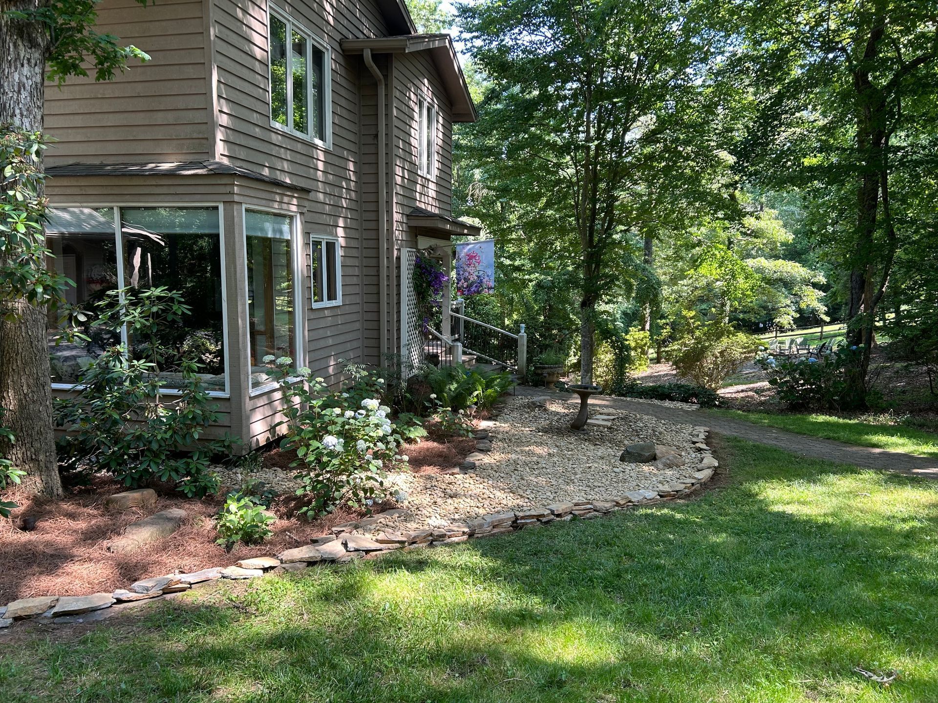 Two-story house with bay window, landscaped yard, and path through trees.