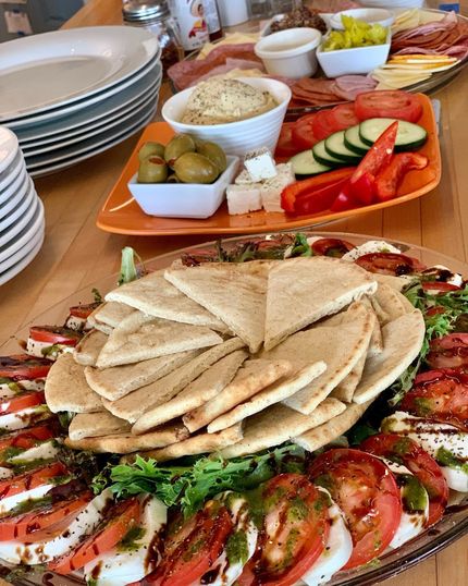Charcuterie board with various foods, including pita bread, cheese, olives, and sliced vegetables.