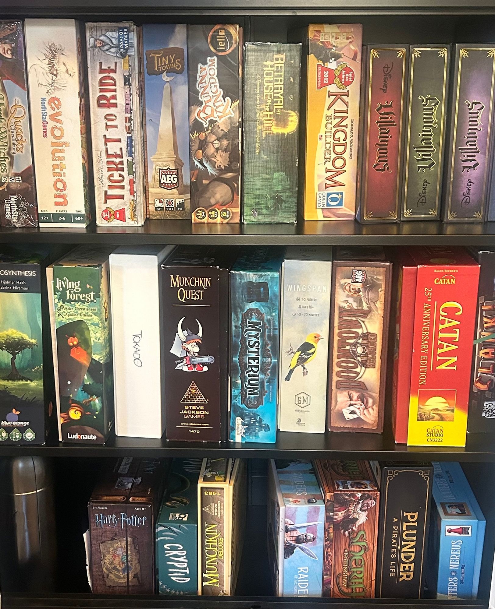 Board game boxes on a black shelf, various sizes and colors. Titles visible, organized.