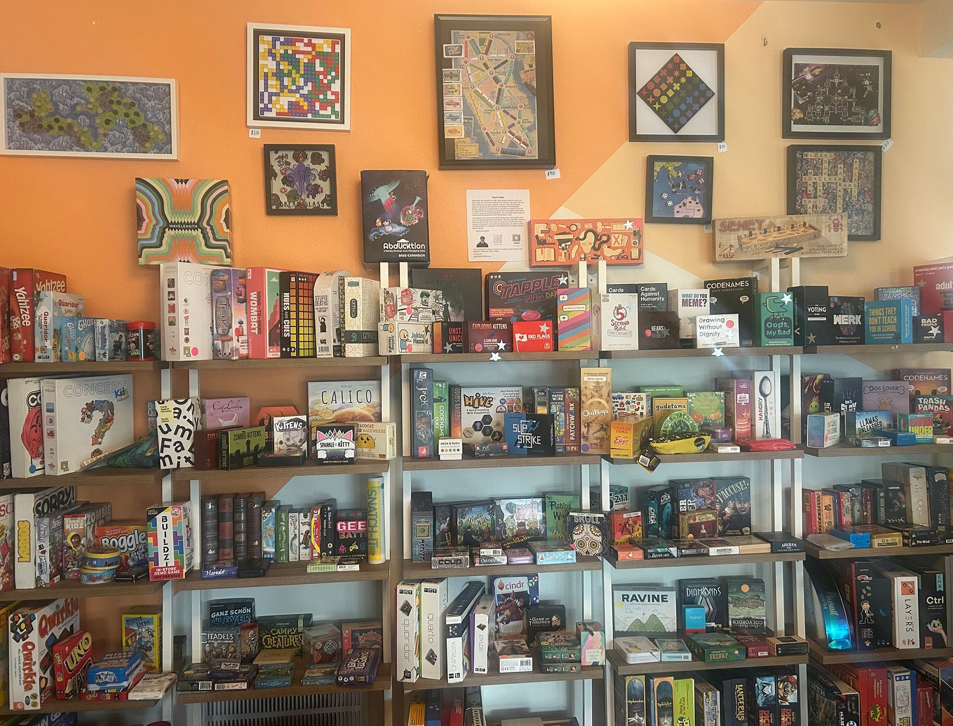 Shelves stocked with board games in a shop, art on the orange wall.