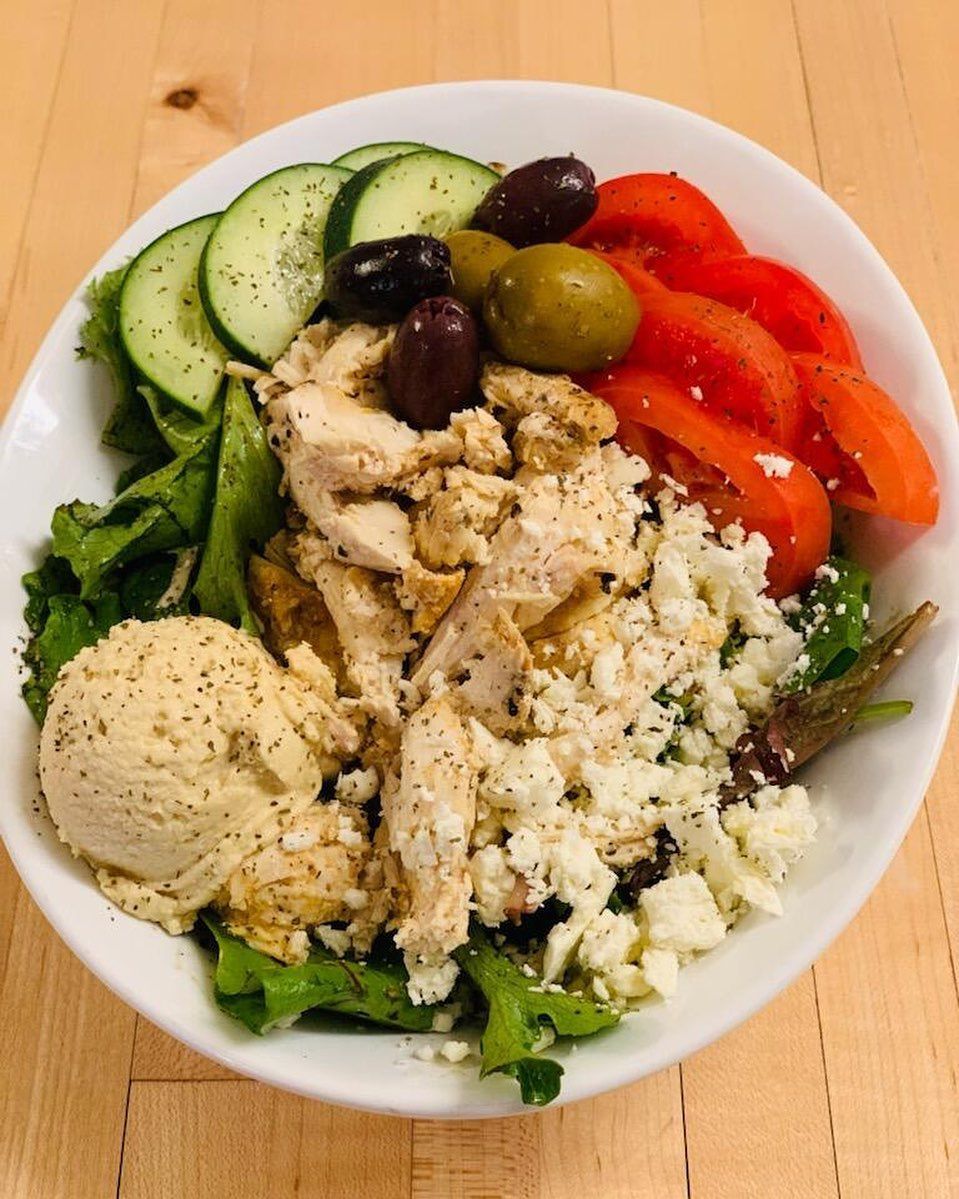 Greek salad bowl with chicken, hummus, tomatoes, cucumbers, olives, and feta.