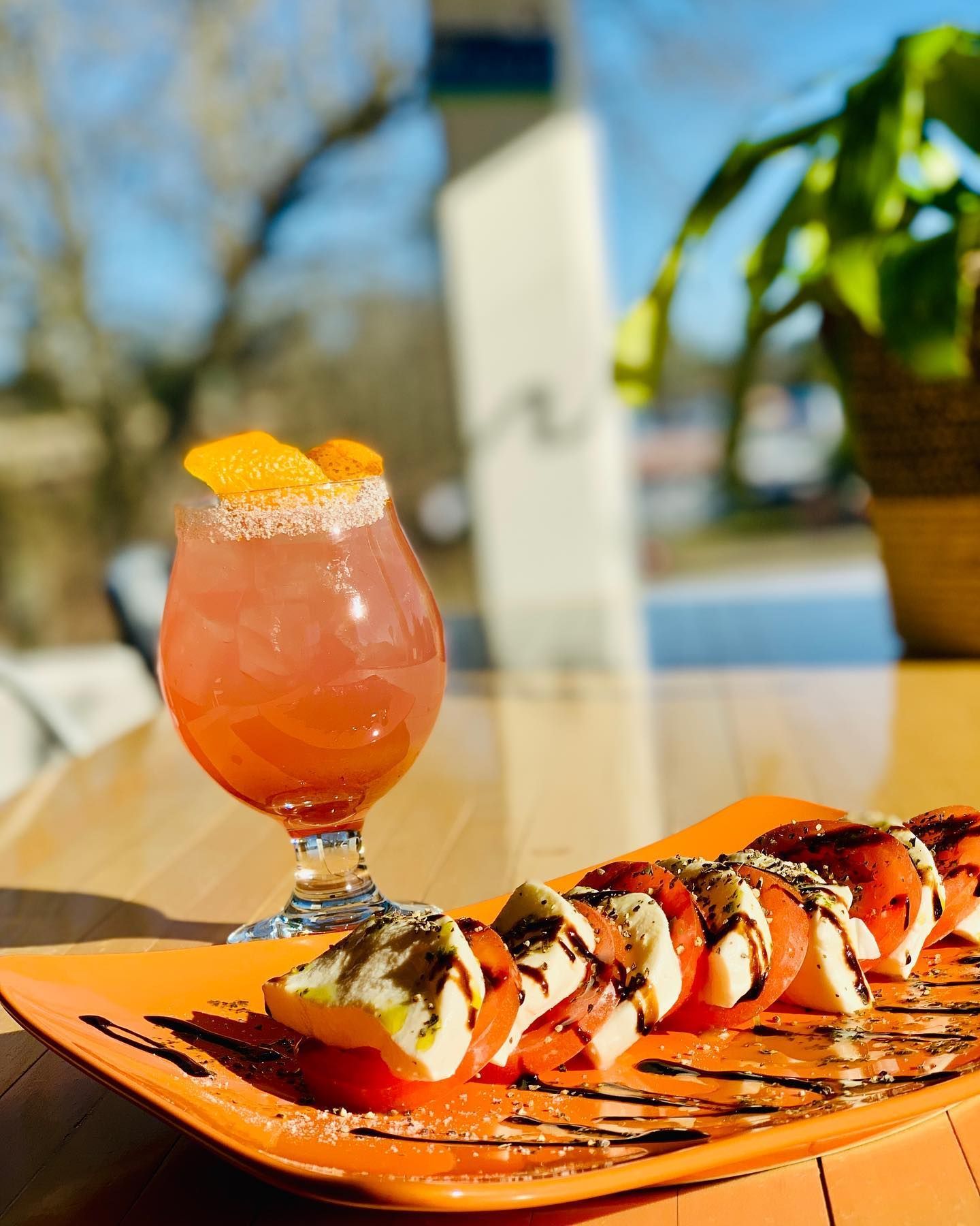 Cocktail and caprese salad on orange plate, bright setting.