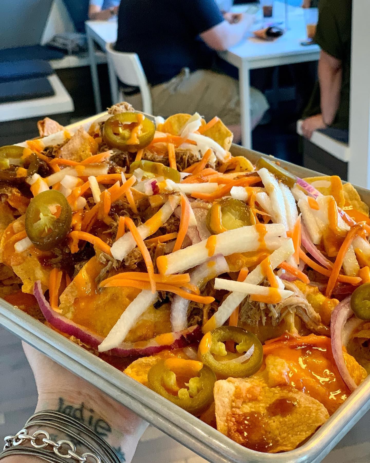Tray of loaded nachos with pulled pork, carrots, pickled jalapeños, and red onion.