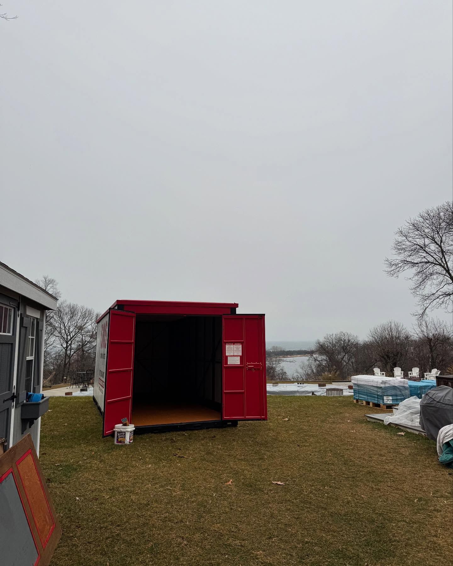 Red storage container with open doors on grassy lawn, cloudy sky background.