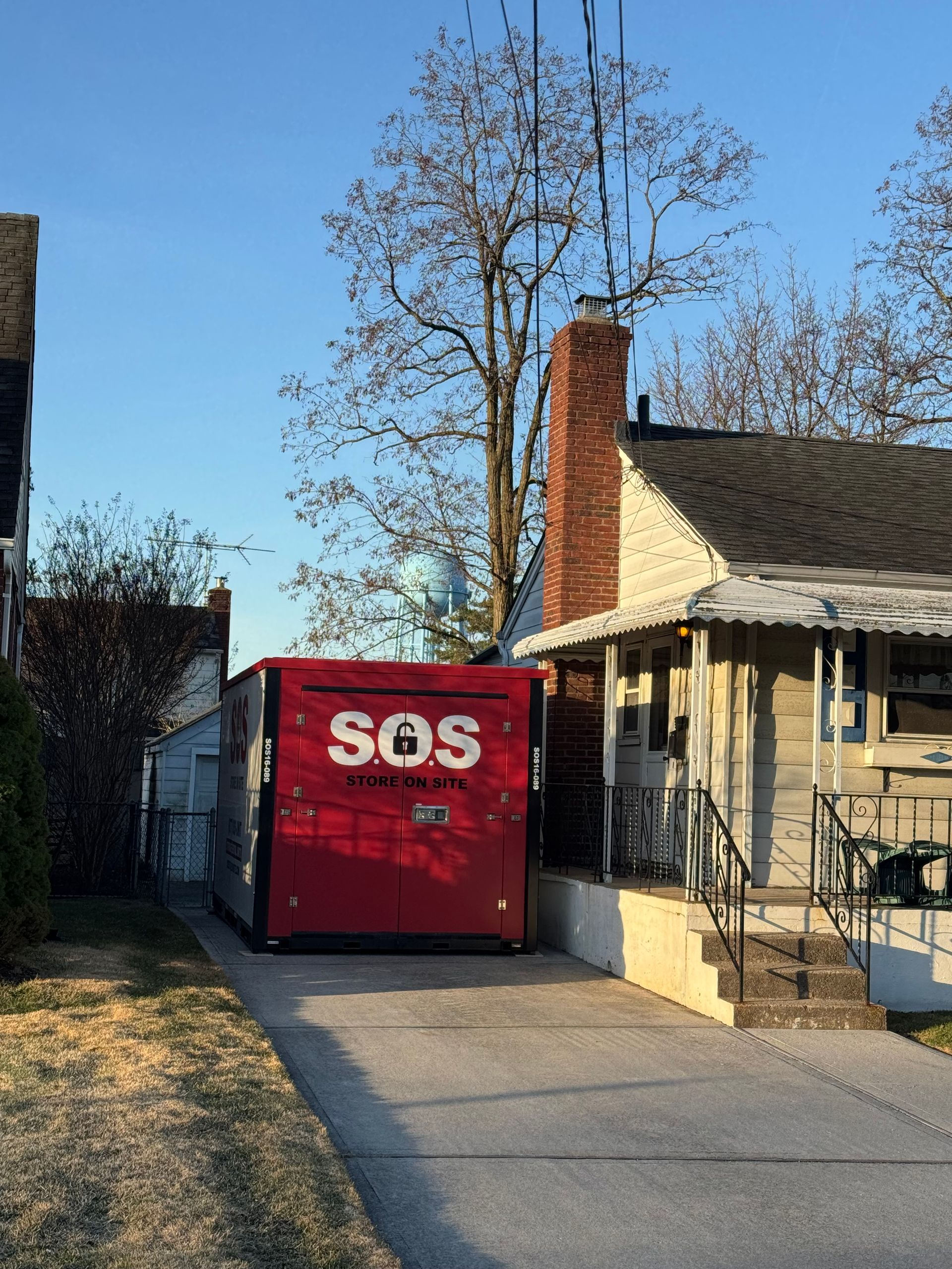 Red SOS industrial generator in a driveway next to a house with a brick chimney and bare trees.