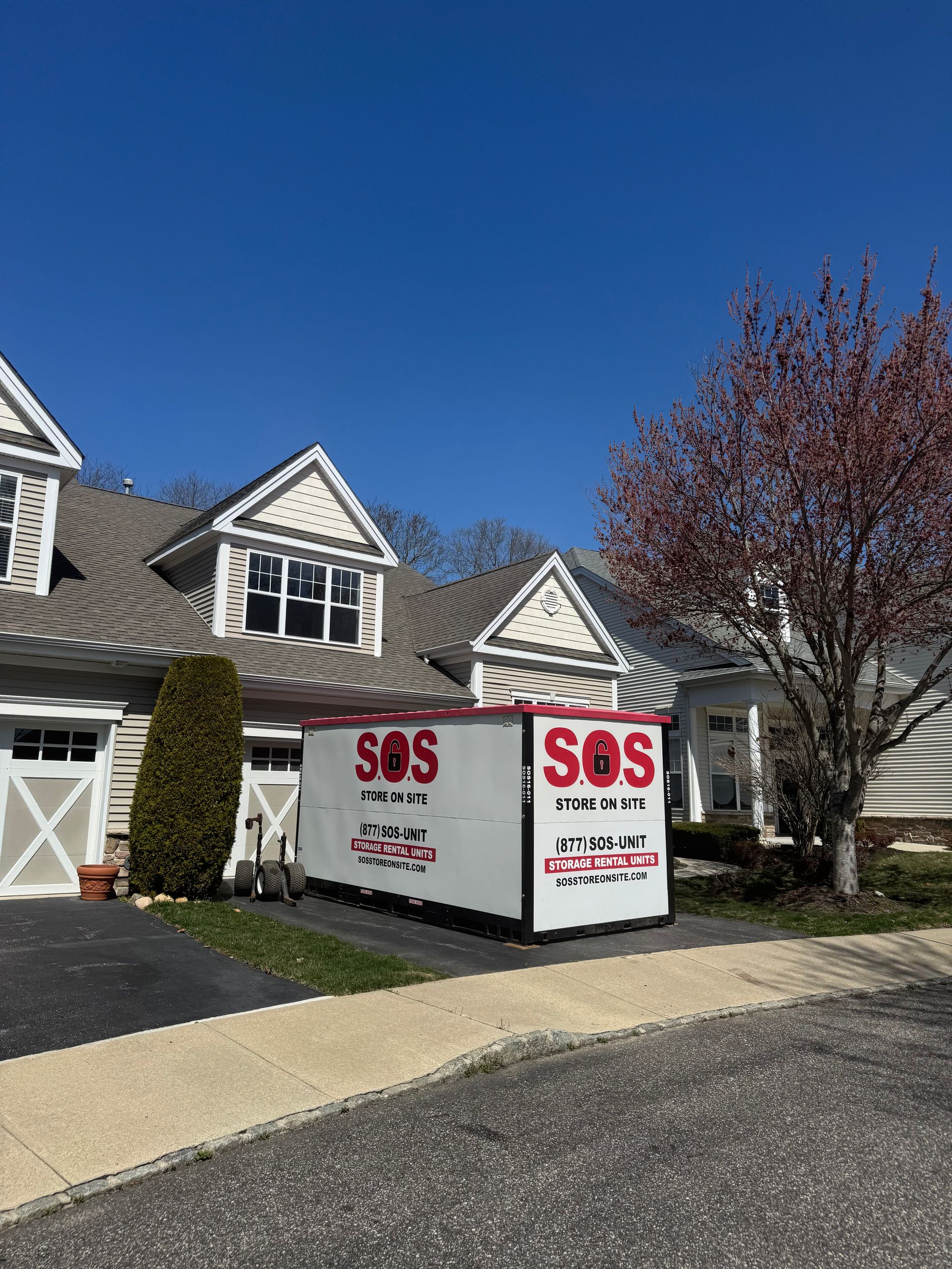 White SOS storage container in front of a townhouse on a sunny day.