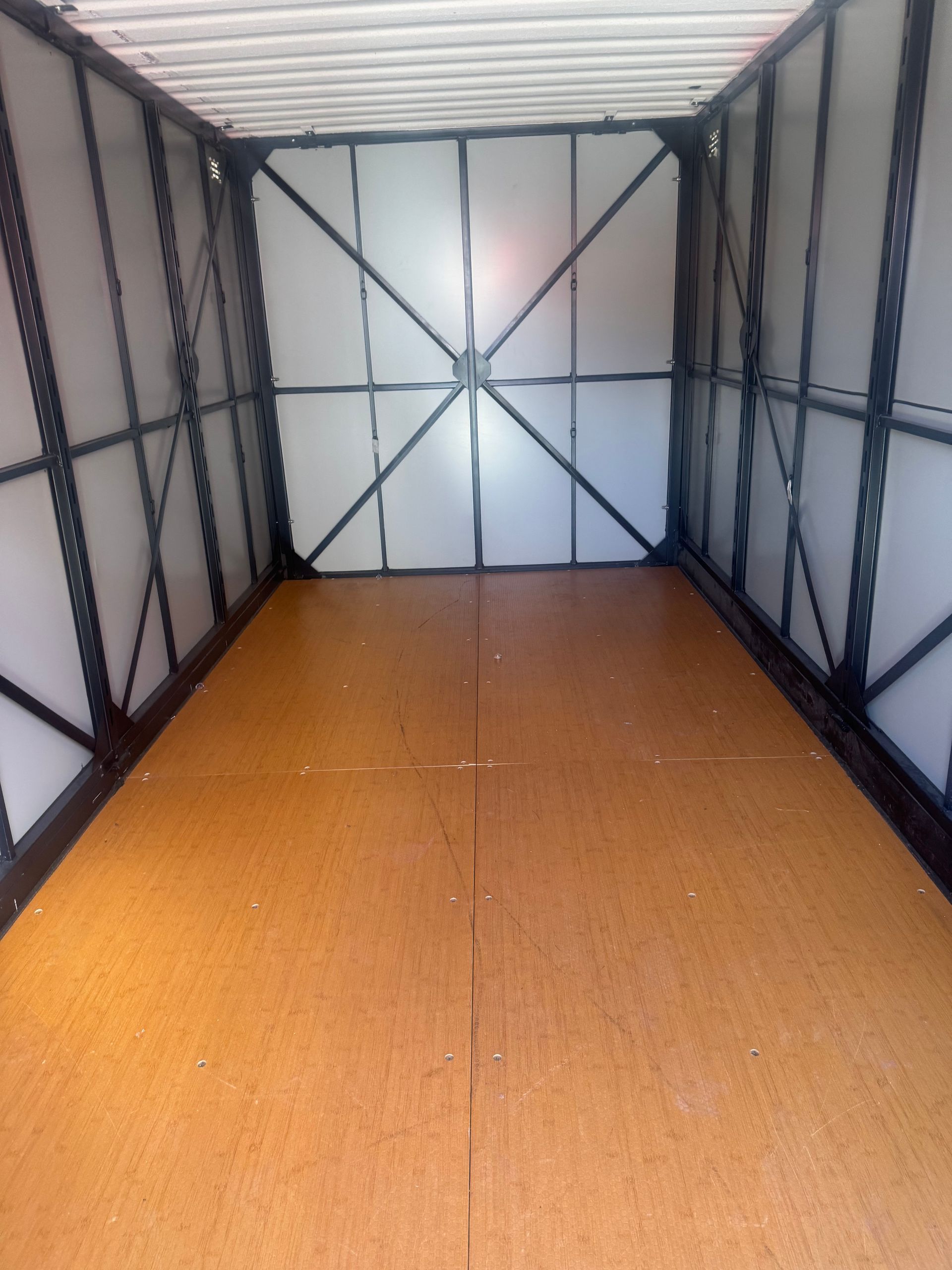 Interior of a cargo container with plywood floor and metal framing. White walls and ceiling.