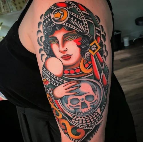 Colorful tattoo of a woman in a headdress holding a skull on an upper arm