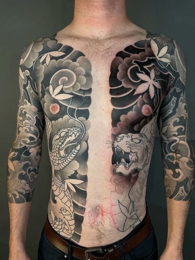 Torso of person with dark floral and koi-style tattoo sleeves, bare chest and abdomen visible