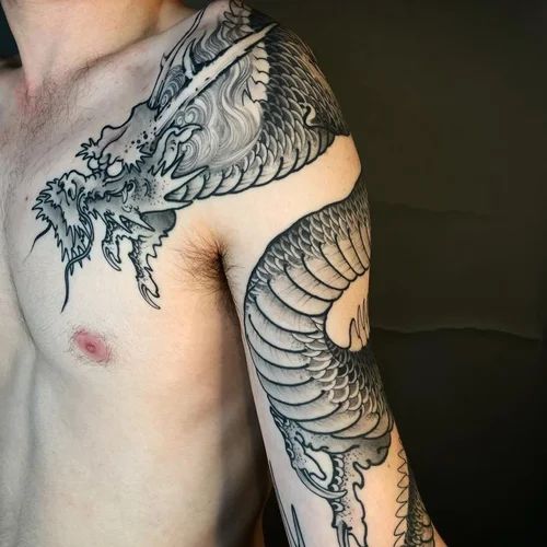Close-up of a shirtless torso and arm with detailed black dragon tattoos on shoulder and upper arm