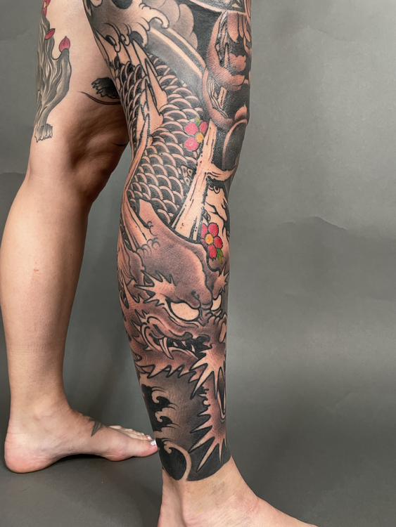 Tattooed lower leg and foot with a large black, red, and pink dragon tattoo against a gray background
