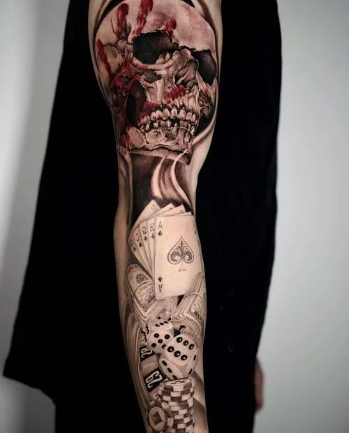 Close-up of a forearm tattoo featuring a skull and playing cards in black and red ink