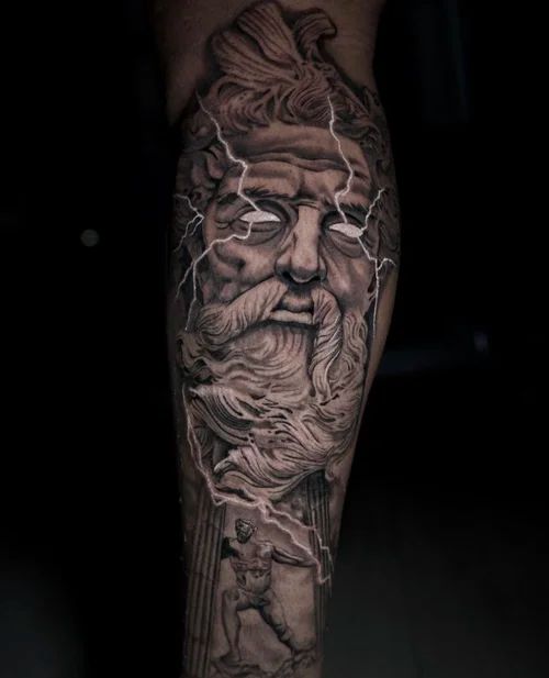 Black-and-gray tattoo of a bearded face on a calf, with flowing hair and lightning-like accents