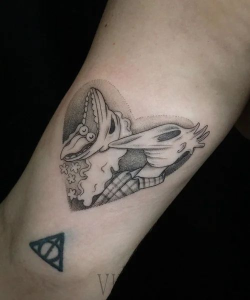Black-and-gray tattoo of an animal head on a forearm, with a small triangle tattoo below.