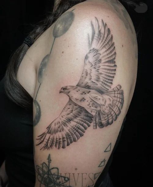 Black-and-gray bird tattoo on an upper arm near other tattoos