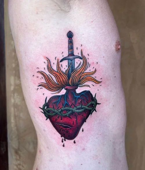 Tattoo of a red heart pierced by a sword, with flames and green vines on skin
