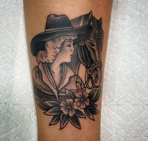 Black-and-gray tattoo of a cowboy beside a horse with flowers on skin